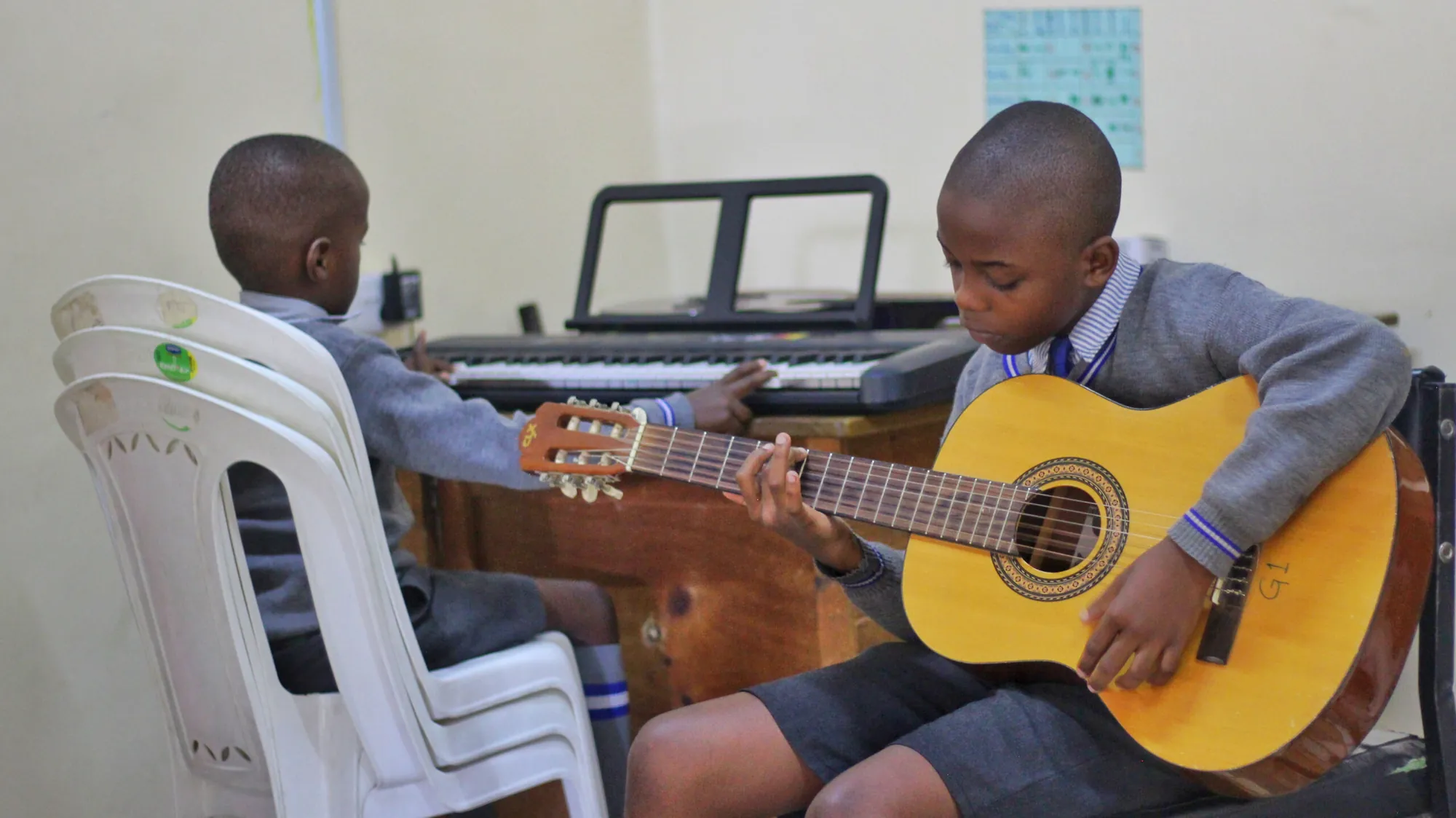 Two boys playing a guitar and a keyboard in a music lesson