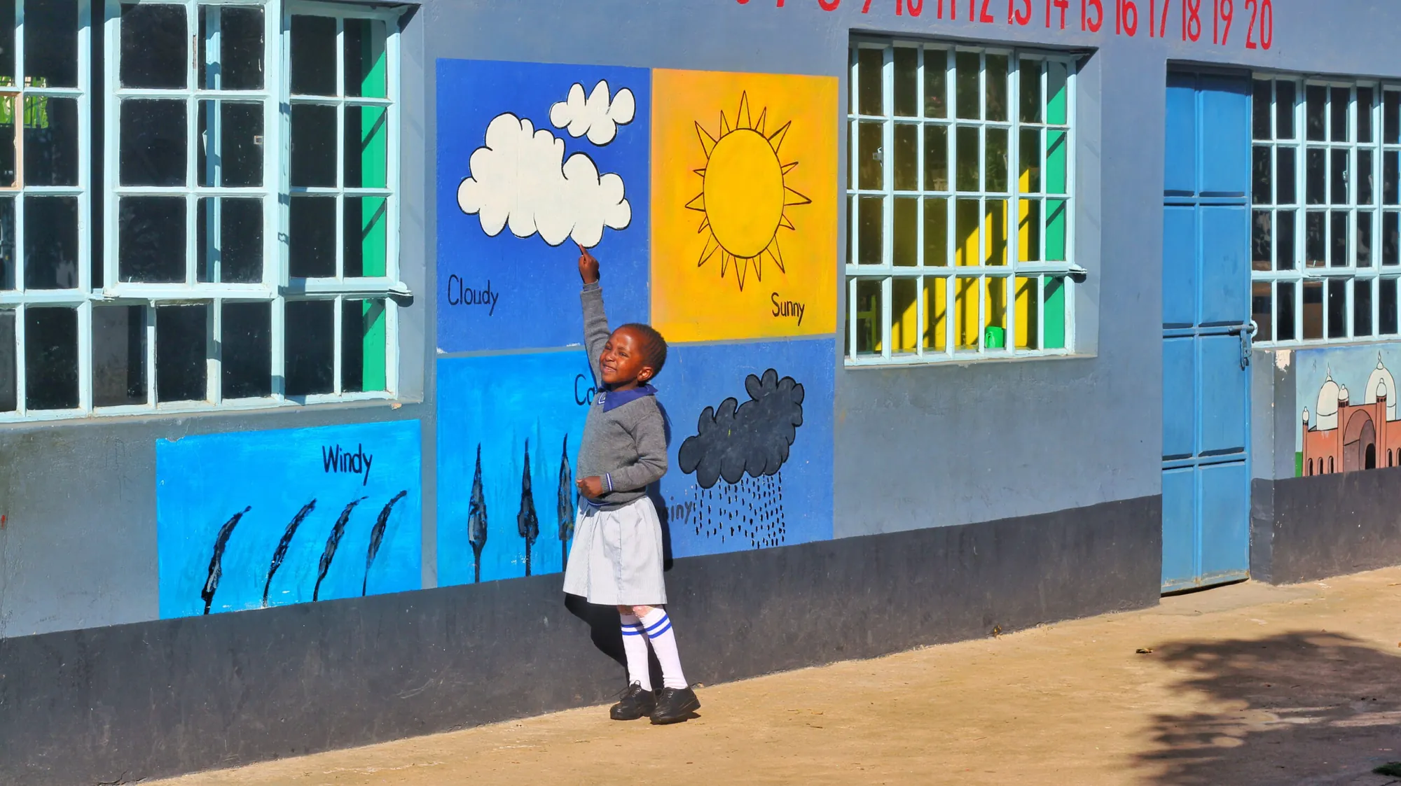 A child touching a painted sun-and-clouds mural on a classroom wall