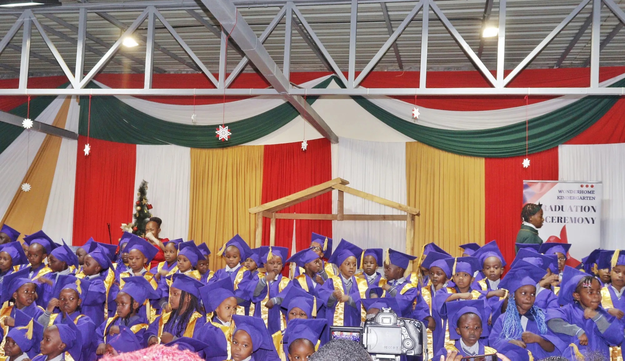 Kindergarten pupils in purple graduation caps seated in a decorated hall