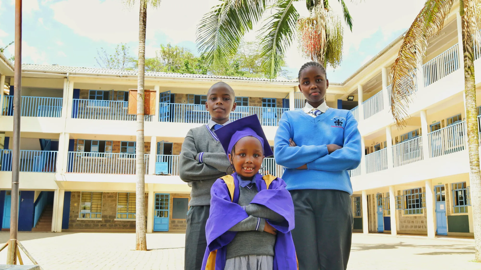 Pupils in uniform and graduation attire standing in the school compound