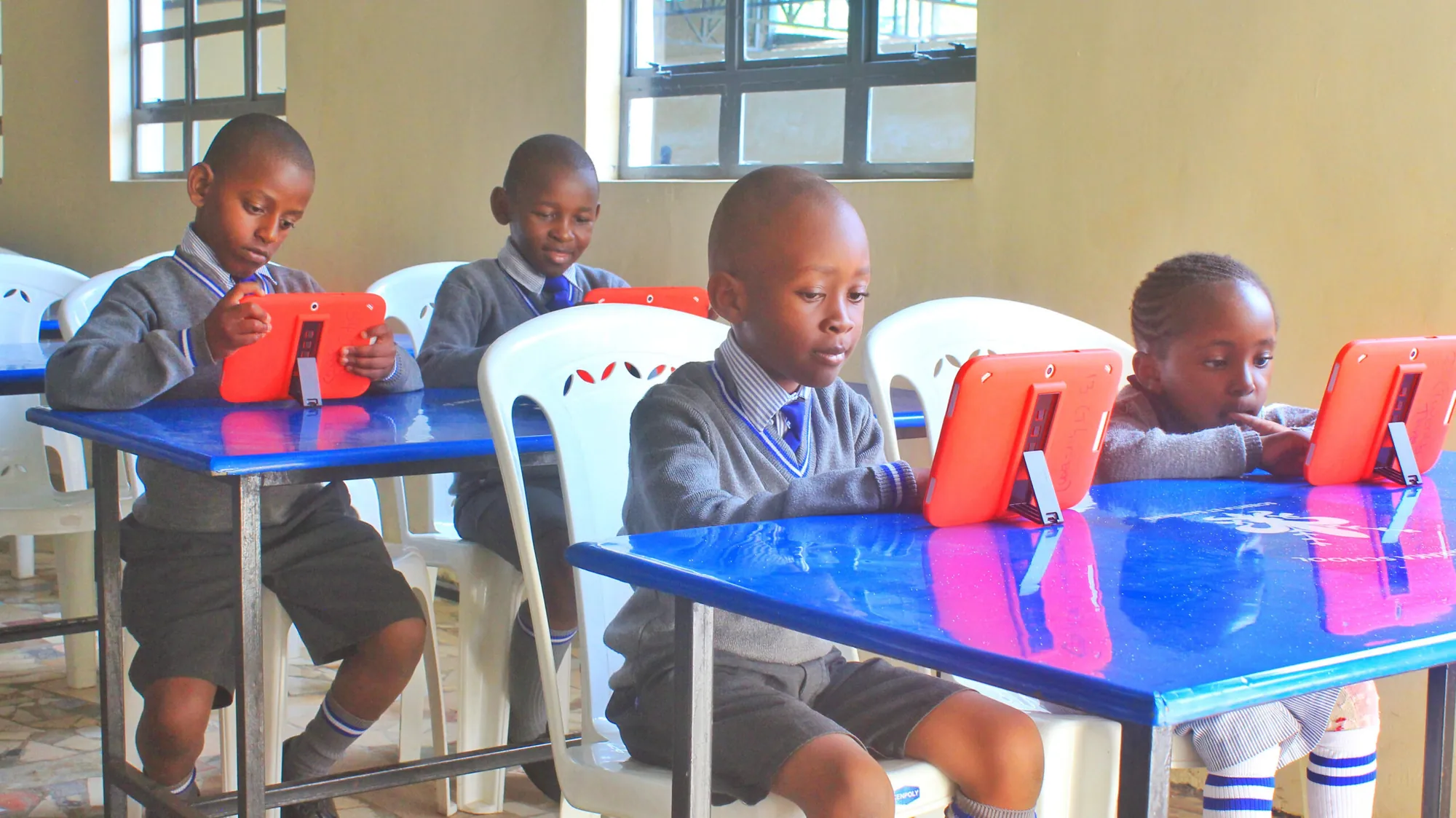 Pupils using tablets at blue desks in a classroom