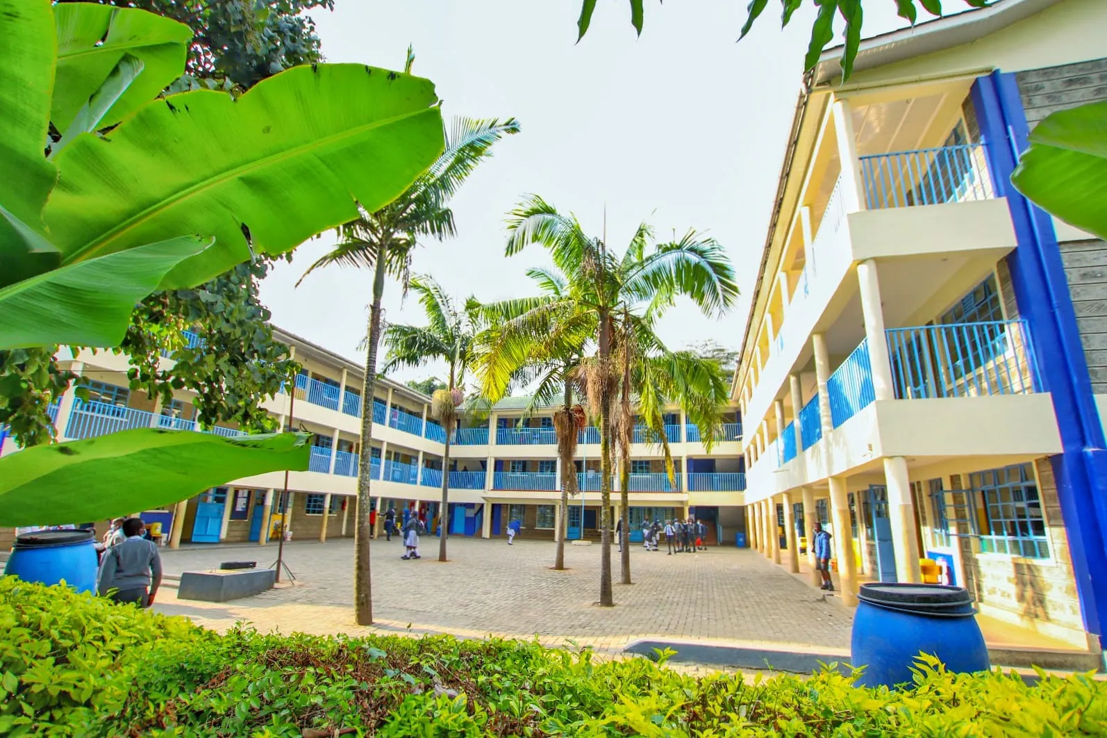Three-storey classroom block with palm trees and a green lawn at St. Mary's Ruaraka School